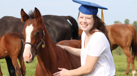 Person in graduation cap standing near a horse